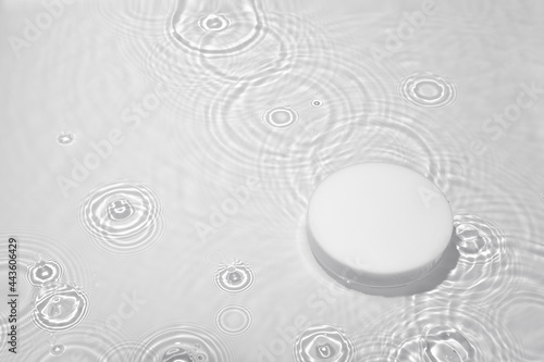 Empty white circle podium on transparent clear calm water texture with splashes and waves in sunlight. Abstract nature background for product presentation. Flat lay cosmetic mockup  copy space.