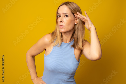 Young woman over isolated yellow background listening to something by putting hand on the ear