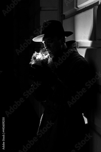 dark dramatic silhouette of a man in a hat Smoking a cigarette on the street at night