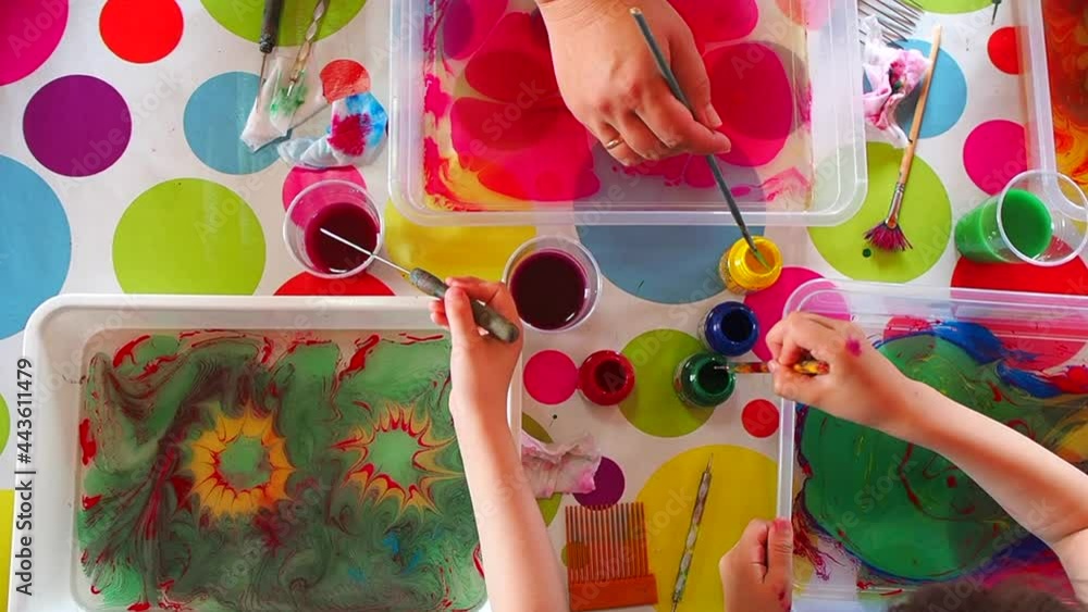 Children draws with paints on water, the Ebru technique, the imprint of the drawing on paper, the childs is engaged in creativity, the teenagers draws an abstract drawing. Top view.