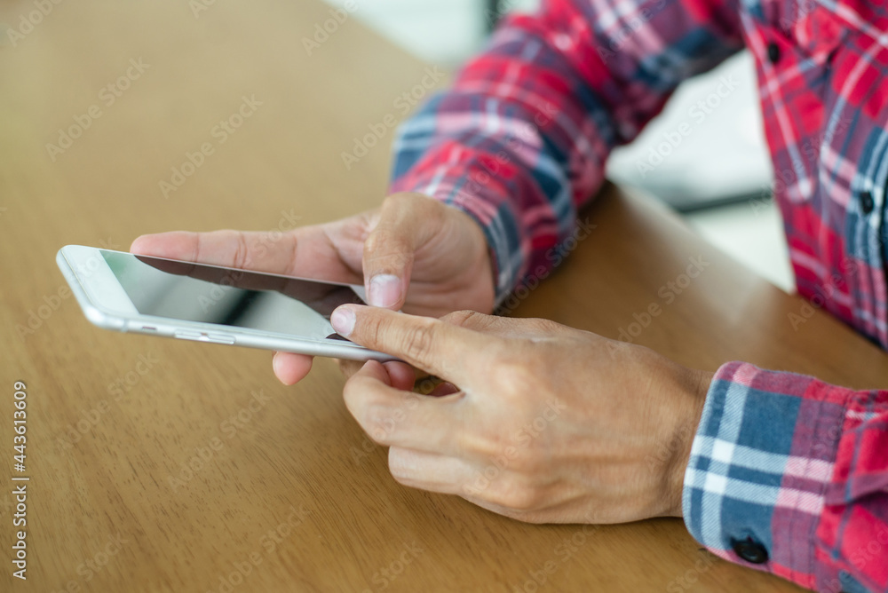 Obraz premium Young man wearing paid shirt hand holding smartphone and checking and replying to emails in the laptop on office desk. He had to work at home due to the coronavirus outbreak.