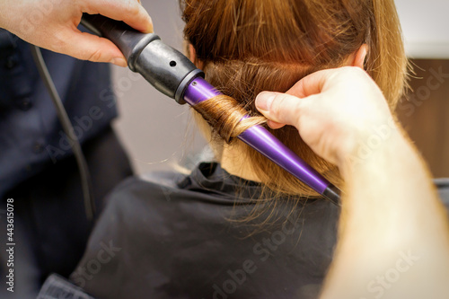 Close up of hairstylist's hands using a curling iron for hair curls in a beauty salon.
