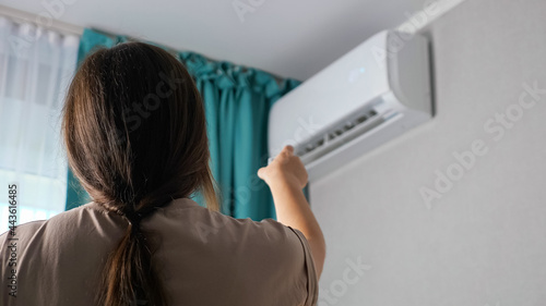 Unrecognizable woman turns on the air conditioner, back view.