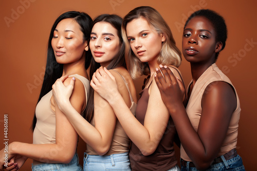 young pretty caucasian, afro, asian, scandinavian woman posing cheerful together on brown background, lifestyle diverse nationality people concept
