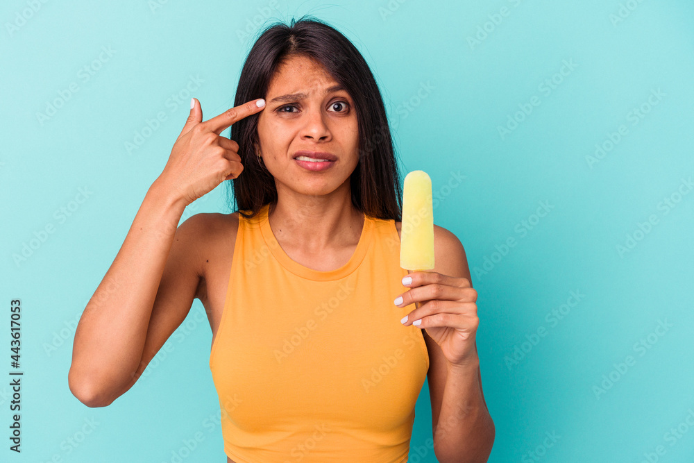 Young latin woman holding ice cream isolated on blue background showing a disappointment gesture with forefinger. Young latin woman holding ice cream isolated on blue background showing a disappointment gesture with forefinger.