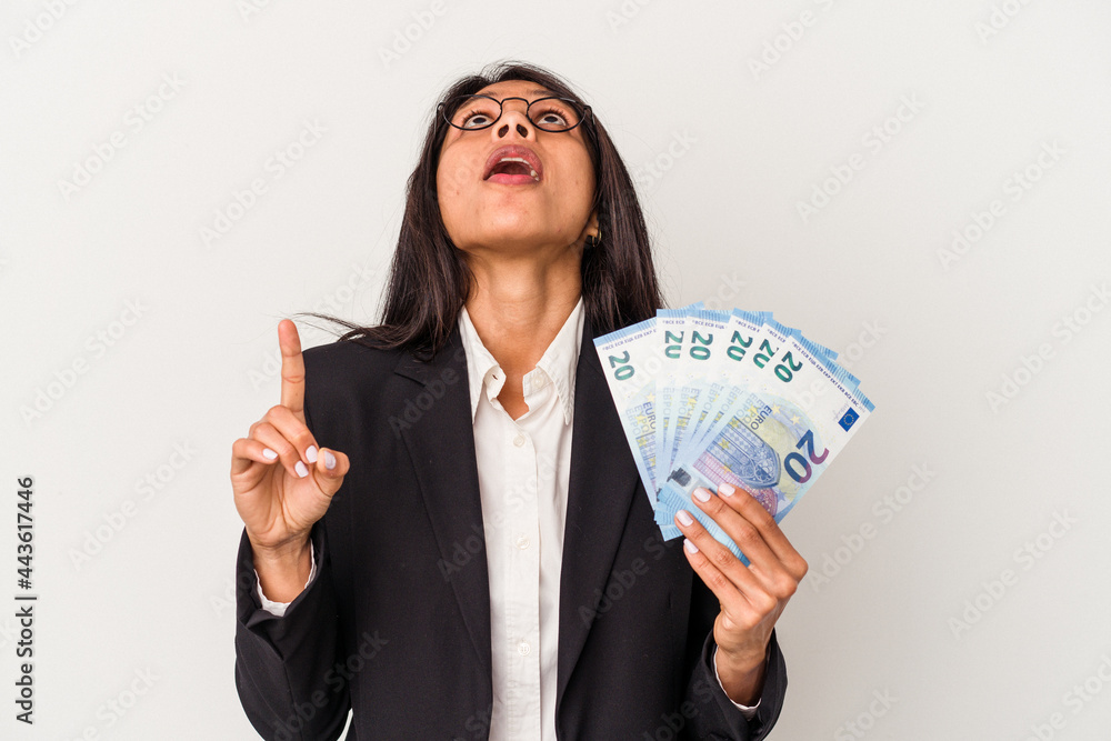 Young business latin woman holding bills isolated on white background pointing upside with opened mouth. Young business latin woman holding bills isolated on white background pointing upside with opened mouth.