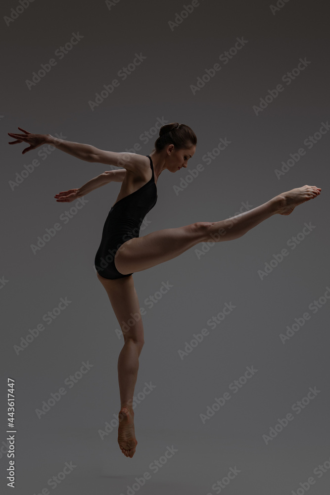 Sideview shot of jumping ballerina against gray background