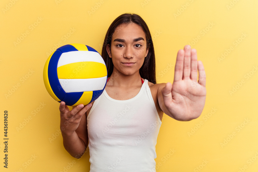 Young mixed race woman playing volleyball on the beach isolated on yellow background standing with outstretched hand showing stop sign, preventing you.