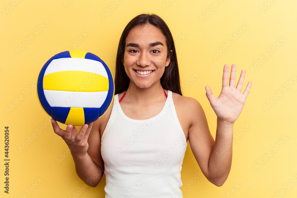 Young mixed race woman playing volleyball on the beach isolated on yellow background smiling cheerful showing number five with fingers. Young mixed race woman playing volleyball on the beach isolated on yellow background smiling cheerful showing number five with fingers.