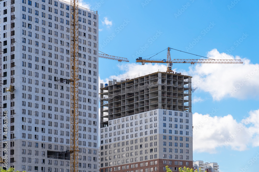 Construction cranes and unfinished residential buildings against clear blue sky. Housing construction, apartment block with scaffolding Construction cranes and unfinished residential buildings against clear blue sky. Housing construction, apartment block with scaffolding