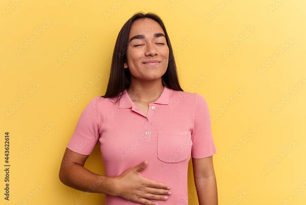 Young mixed race woman isolated on yellow background touches tummy, smiles gently, eating and satisfaction concept. Young mixed race woman isolated on yellow background touches tummy, smiles gently, eating and satisfaction concept.
