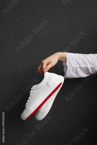 White sneakers with red sole in female hand at black background