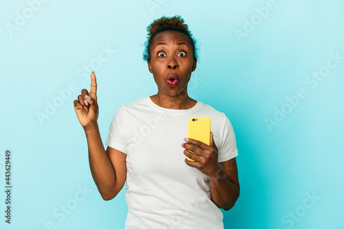 Foto Young african american woman holding a mobile phone isolated on blue background having some great idea, concept of creativity