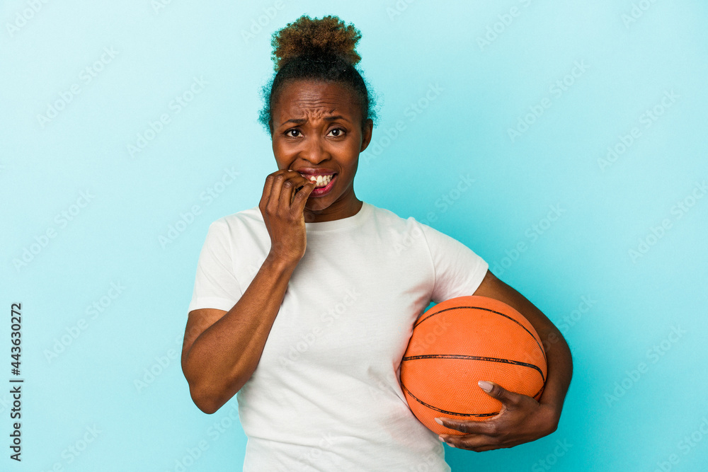 Young african american woman playing basketball isolated on blue background biting fingernails, nervous and very anxious. Young african american woman playing basketball isolated on blue background biting fingernails, nervous and very anxious.