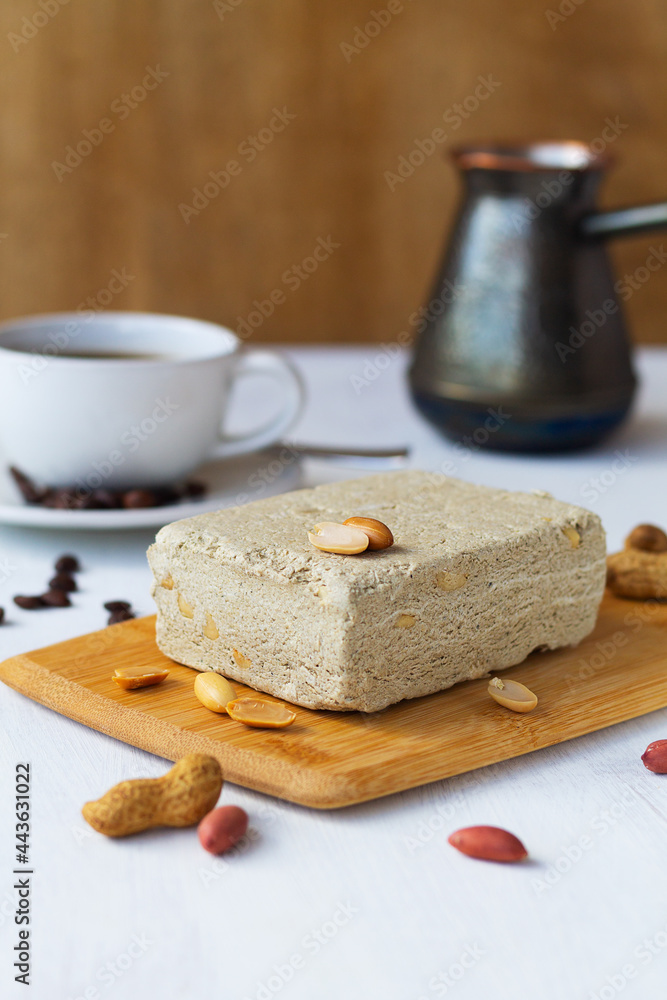 halwa from sunflower seeds with peanut on the wood cutting board. tasty dessert. national traditional sweetness of Turkish and arabic halva with cup of coffee on the white table. vertical. copy space