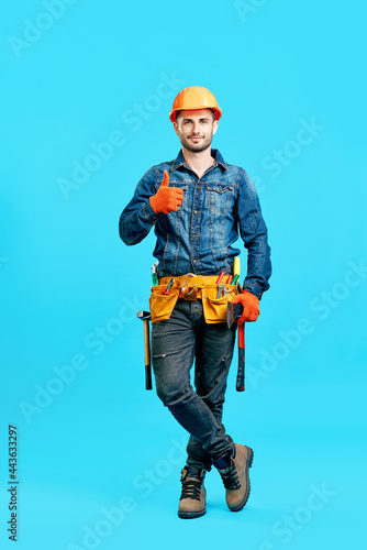 Full length portrait of confident handsome male construction worker in safety helmet showing thumbs up sign