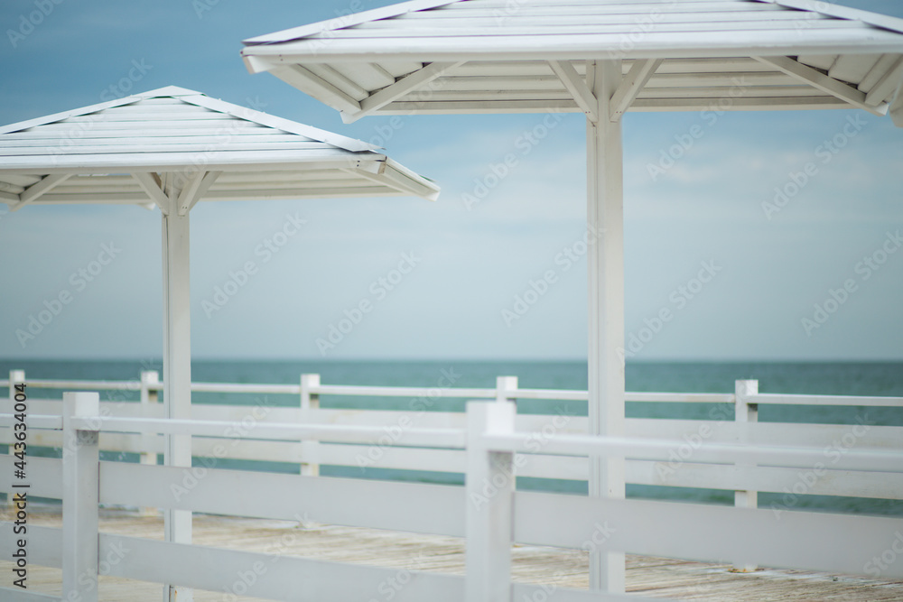 White wooden pier with mushrooms from the sun against the background of the sea and blue sky with clouds