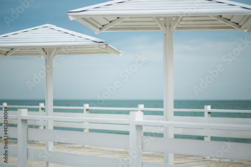 White wooden pier with mushrooms from the sun against the background of the sea and blue sky with clouds © Svitlana