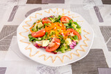 Vegetable and lettuce salad with sliced tomato, grated carrot, diced cucumber and white plate on gray-toned tablecloth