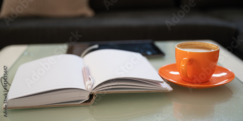 Open notepad with pen in the middle  cup of coffee and digital tablet on coffee table