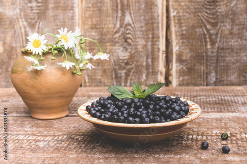 Ceramic plate with fresh berry blueberries on a wooden background and a bouquet of daisies in a vase