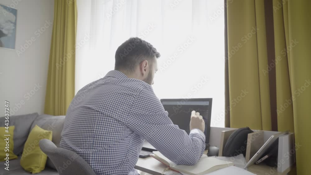 Male trader in formalwear looking at trading charts and taking notes, working from home Male trader in formalwear looking at trading charts and taking notes, working from home