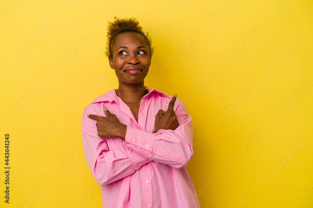Young african american woman isolated on yellow background points sideways, is trying to choose between two options. Young african american woman isolated on yellow background points sideways, is trying to choose between two options.