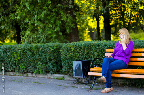 Defocus elegance caucasian blond woman talking, speaking on the phone outside, outdoor. 40s years old woman in purple blouse in park. Adult women using mobile phone. Copy space. Out of focus