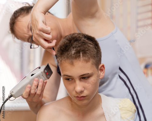 Cutting the hair of a boy, young guy at home due to the lockdown and quarantine coronavirus epidemic. Parents and relatives help each other get their hair without going to the hairdresser