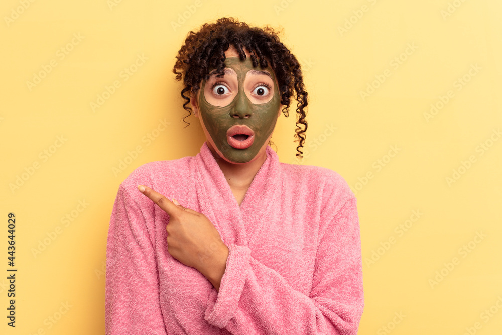 Young mixed race wearing facial mask isolated on yellow background pointing to the side
