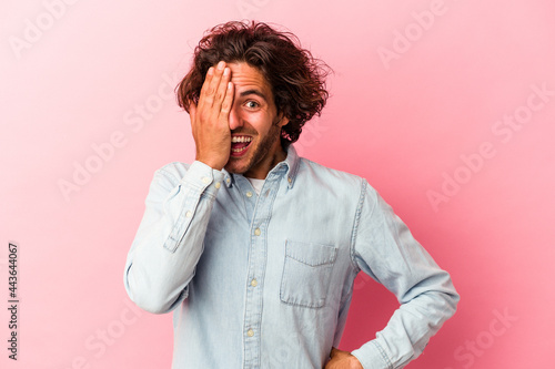 Young caucasian man isolated on pink bakcground having fun covering half of face with palm.