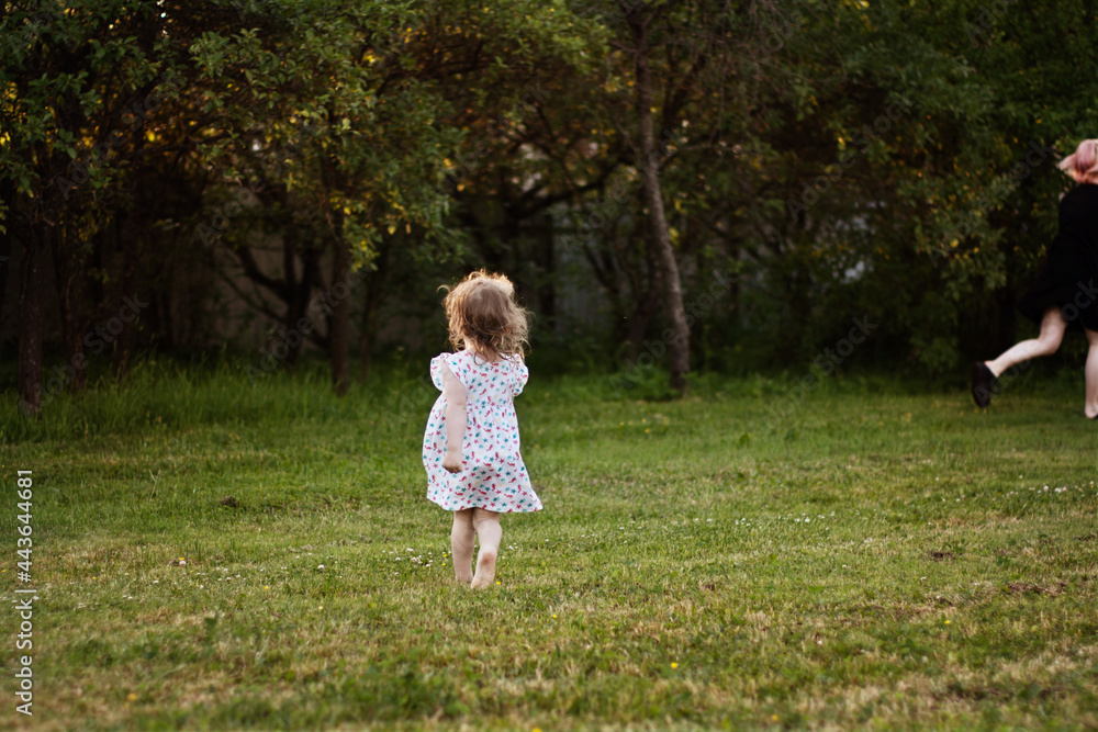 the baby runs through the summer garden. a little girl runs away on the green grass the baby runs through the summer garden. a little girl runs away on the green grass