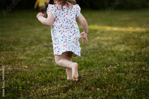 the bare feet of a little girl in a white dress. the child quickly runs away in the summer on the grass barefoot