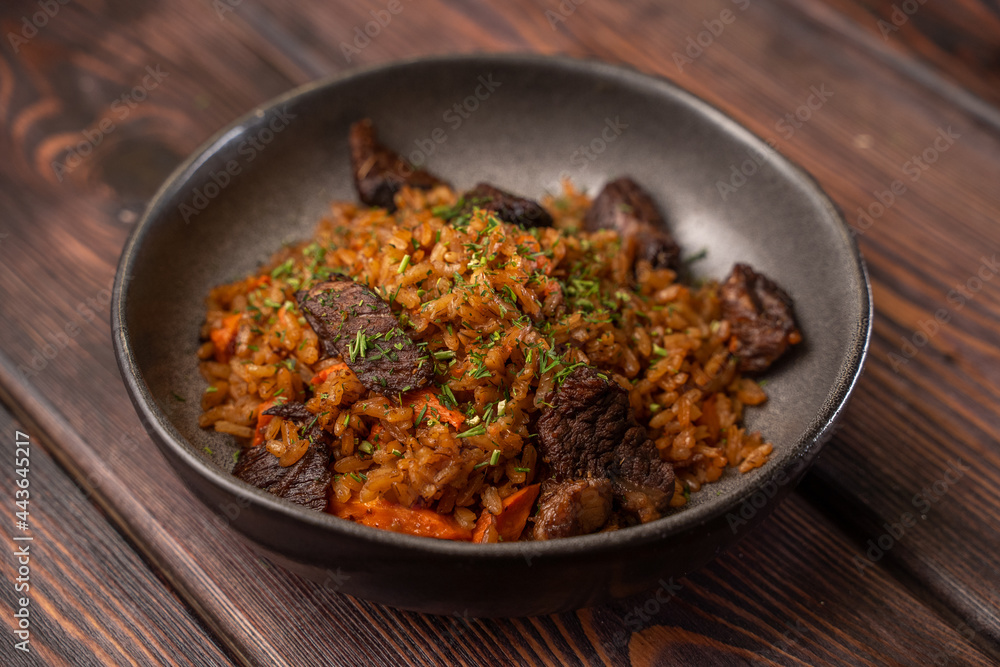 Traditional pilaf with meat in a black plate on a wooden background Traditional pilaf with meat in a black plate on a wooden background