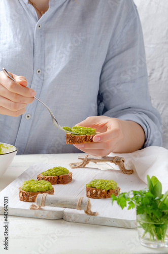 Female hand holds fork and put avocado cream on bread brown. 