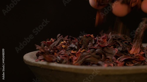 A males hand touches and feels hibiscus tea leaves on clay plate with dark background