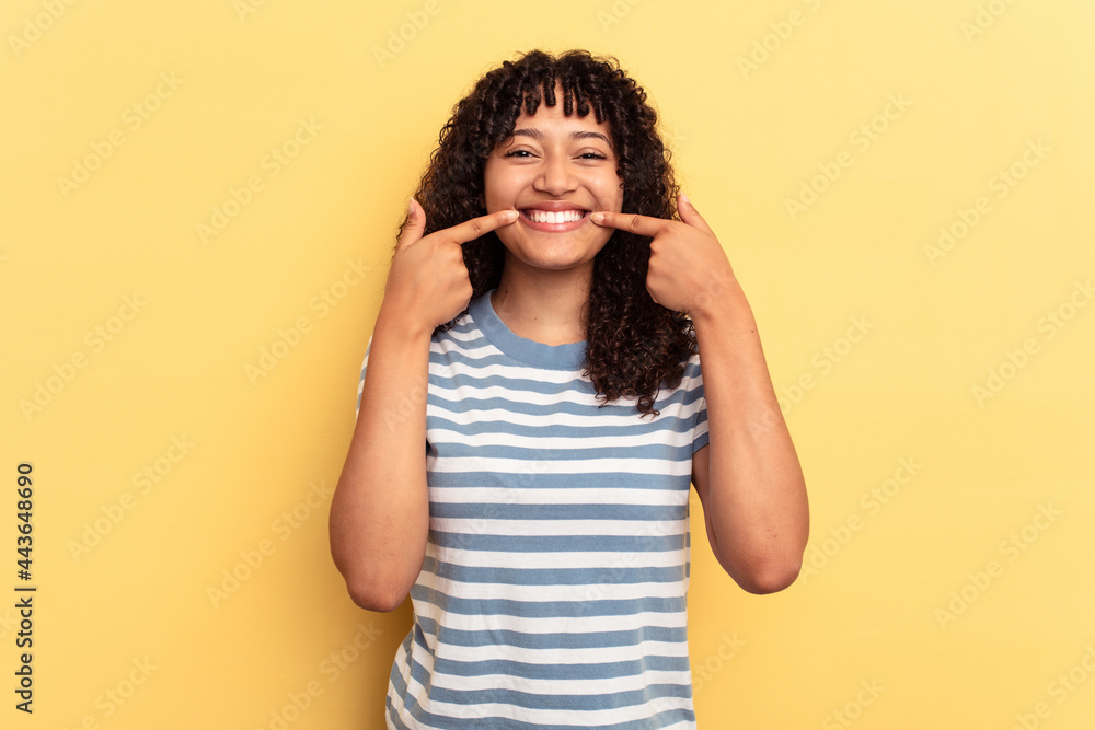 Young mixed race woman isolated on yellow background smiles, pointing fingers at mouth. Young mixed race woman isolated on yellow background smiles, pointing fingers at mouth.