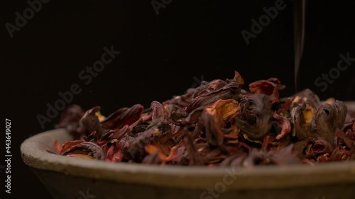 Hibiscus tea leaves sprinkled on clay plate with dark background 