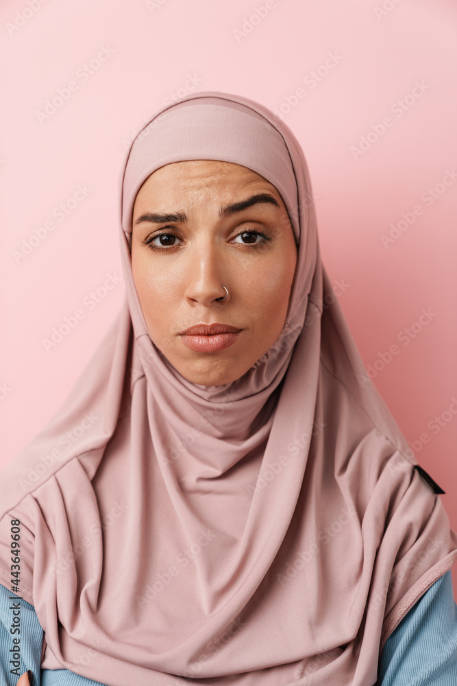 A portrait of the thinking muslim woman wearing pink hijab and raising an eyebrow in the pink studio A portrait of the thinking muslim woman wearing pink hijab and raising an eyebrow in the pink studio