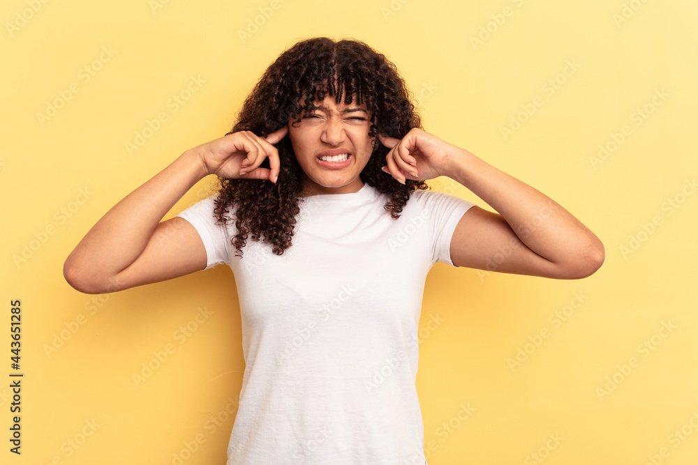 Young mixed race woman isolated on yellow background covering ears with fingers, stressed and desperate by a loudly ambient. Young mixed race woman isolated on yellow background covering ears with fingers, stressed and desperate by a loudly ambient.