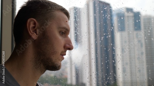 Quarantine effects on physical and mental well-being. Side view of a man putting his head against the window on a rainy day