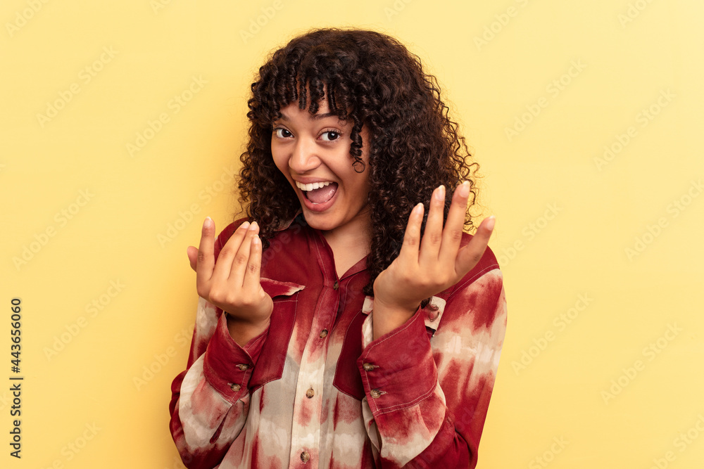 Young mixed race woman isolated on yellow background pointing with finger at you as if inviting come closer. Young mixed race woman isolated on yellow background pointing with finger at you as if inviting come closer.