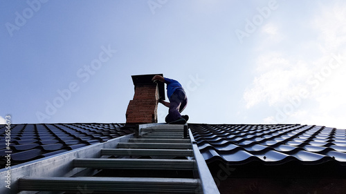 Fotografie, Obraz a chimney sweep climbs a metal ladder to the roof of the bathhouse to clean the