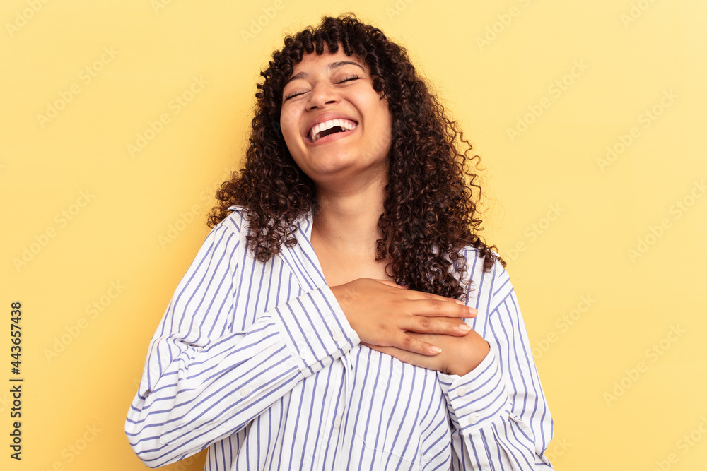 Young mixed race woman isolated on yellow background laughing keeping hands on heart, concept of happiness. Young mixed race woman isolated on yellow background laughing keeping hands on heart, concept of happiness.