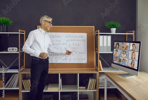 The senior male teacher conducts a class on the principle of online education with his students. An older man in a white shirt, black pants, and glasses shows a mathematical graph.