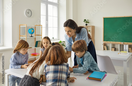 Young caucasian teacher teaching schoolchildren or preschooler group in classroom talking and showing task. Education and learning, elementary school or kindergarten preschool kids development