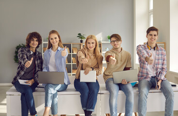 Group of happy high school, college or university students with laptops and tablets looking at camera, smiling and giving thumbs-up all together. Excellent choice of education course, success concept