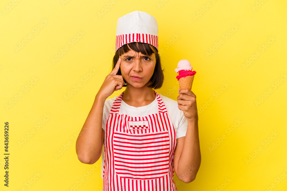 Young mixed race ice cream maker woman holding an ice cream isolated on yellow background pointing temple with finger, thinking, focused on a task. Young mixed race ice cream maker woman holding an ice cream isolated on yellow background pointing temple with finger, thinking, focused on a task.