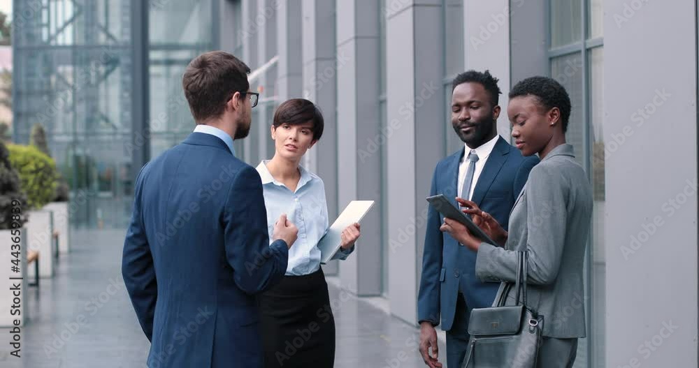 Concept of successful team work. Portrait of cheerful business diverse colleagues standing at the street near their office and discussing work and plans Concept of successful team work. Portrait of cheerful business diverse colleagues standing at the street near their office and discussing work and plans