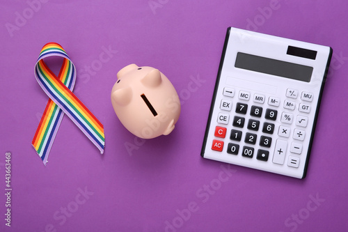 Calculator with piggy bank and LGBT rainbow ribbon pride tape symbol on purple background. Top view photo